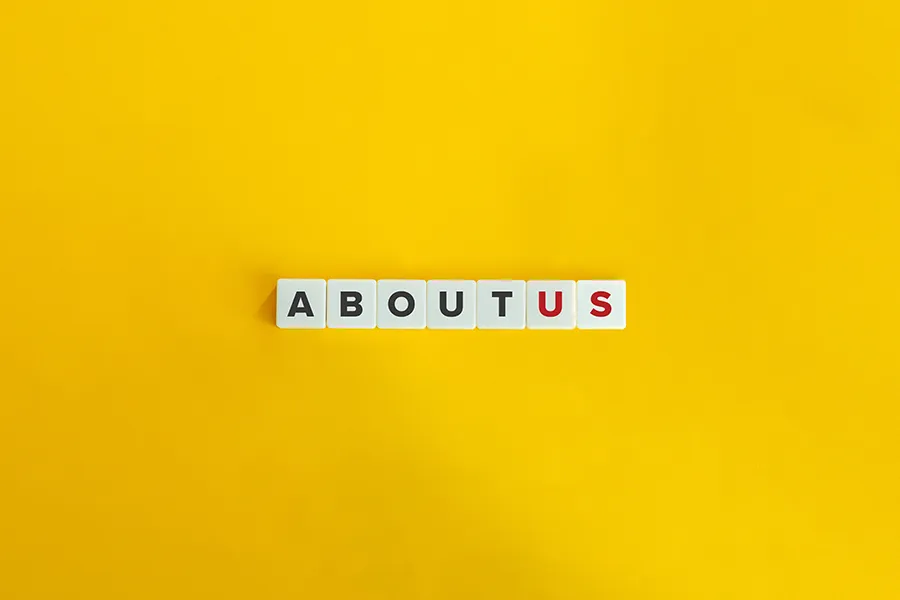 Minimalist “About Us” concept with white letter tiles spelling ABOUT US centered on a bright yellow background.